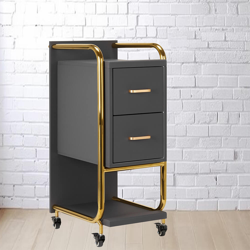 A black and gold metal cart with two drawers and wheels, set against a white brick wall.